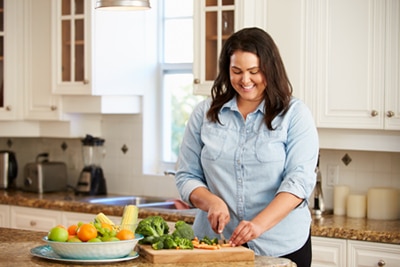 A smiling young woman chopping vegetables in her kitchen