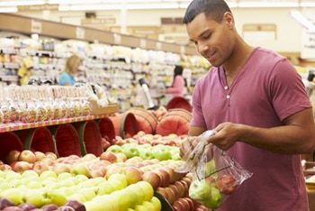 A man putting apples into a bag at the grocery store