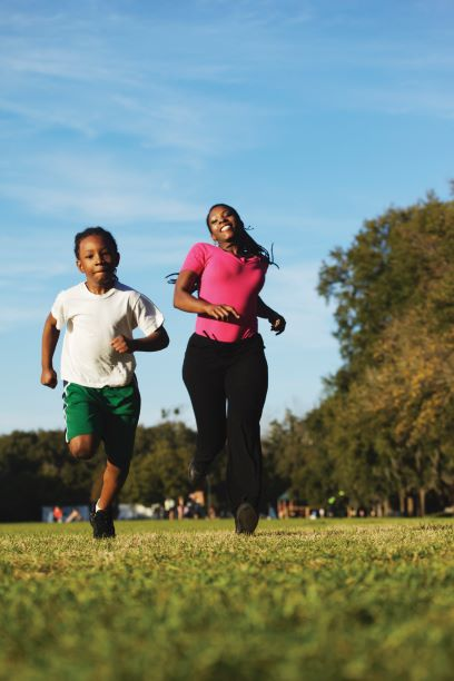 A mother and son run side by side on a grassy field.